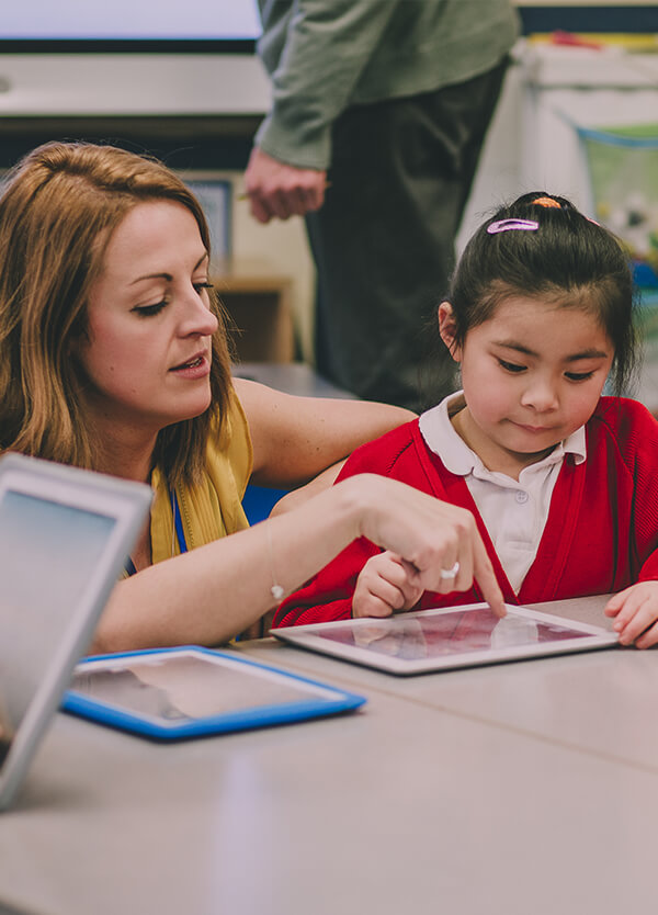 A teacher points to a tablet screen before a young child